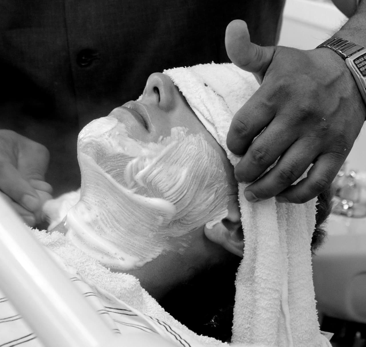 Hot towel folded over a customer's face in the chair, in black and white