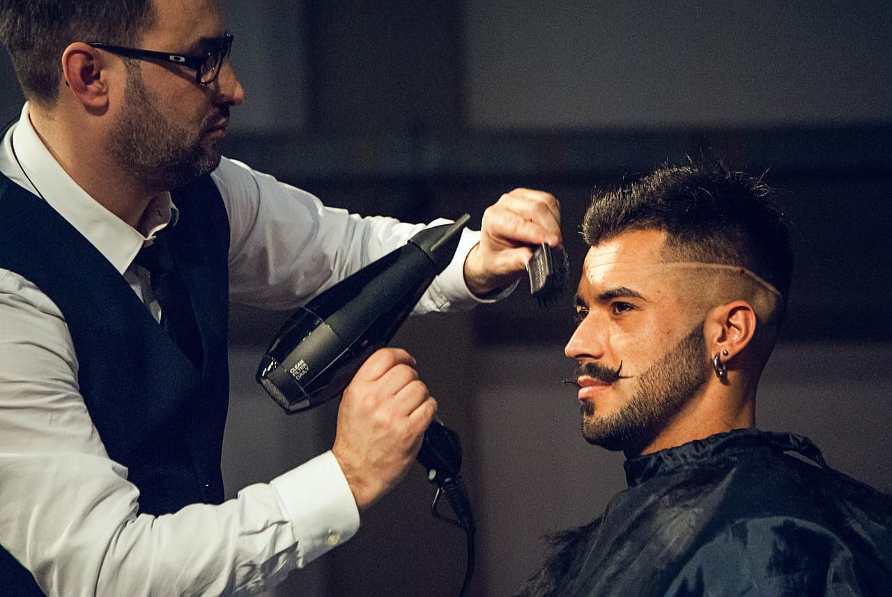 Barber in a waistcoat drying a fresh skin fade with a parting line into shape