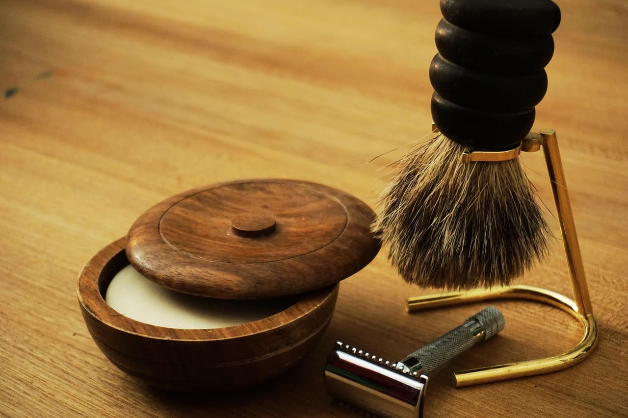 Shaving bowl, brush on a brass stand and a safety razor on a wooden counter